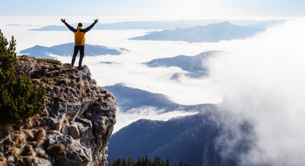 Mann steht am Berg, unter ihm Nebel