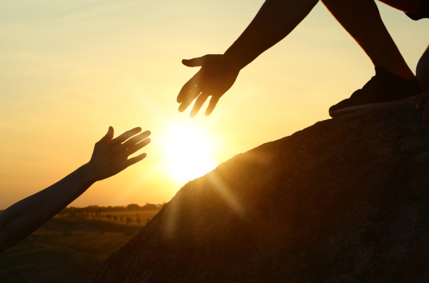 Jemand streckt einem anderen die Hand entgegen, Sonnenuntergang