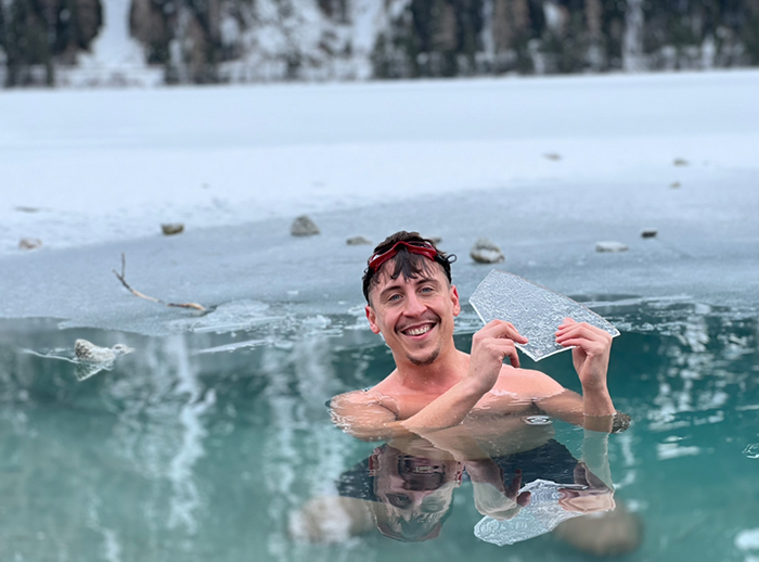 Ein Mann beim Eisbaden im See, wie er eine Eisplatte hochhält